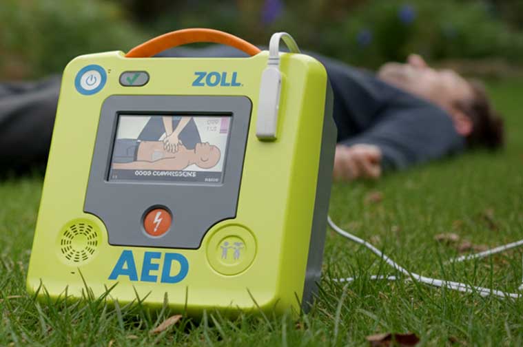 Ein Defibrillator vor einem bewusstlosen Mann im Rasen liegend